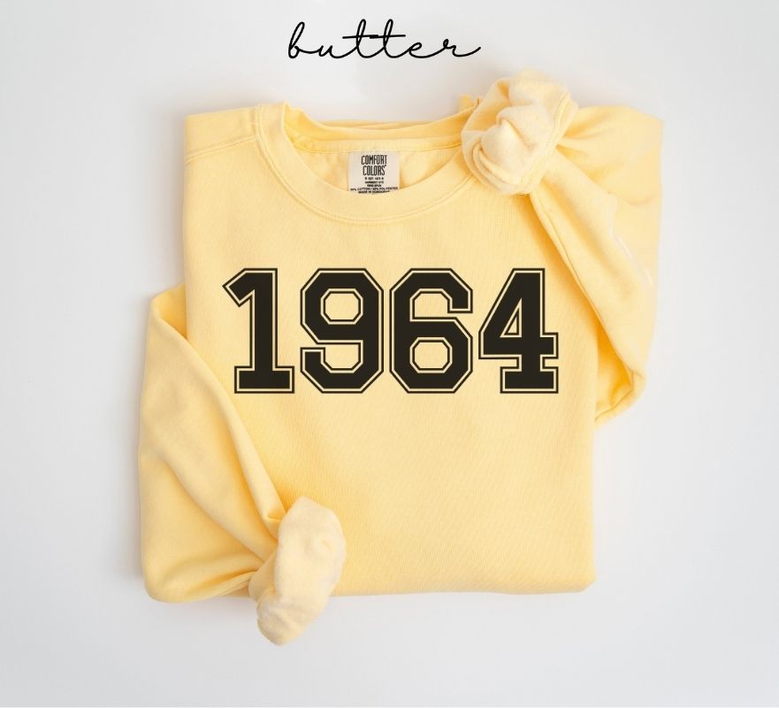 Yellow (butter) sweatshirt with '1964' printed on it, folded and displayed against a white background.
