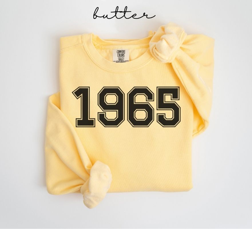 Yellow (butter) sweatshirt with '1965' printed on it, folded and displayed against a white background.
