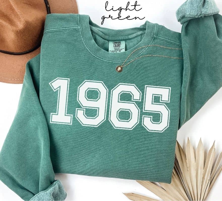 Light green sweatshirt with '1965' printed on it, displayed on a white background.
