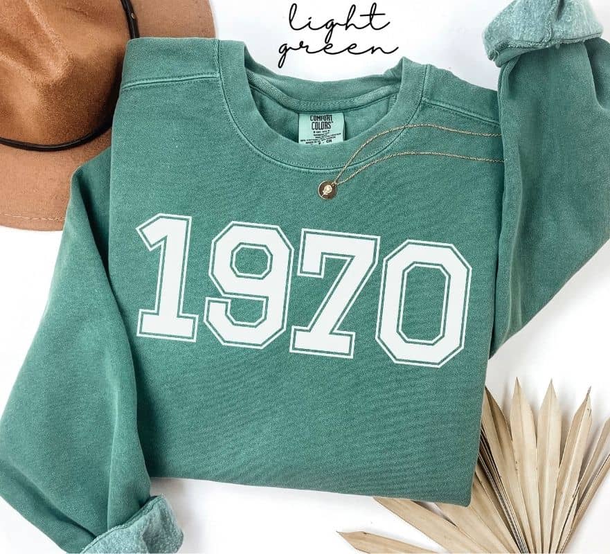Light green sweatshirt with '1970' printed on it, displayed on a white background.