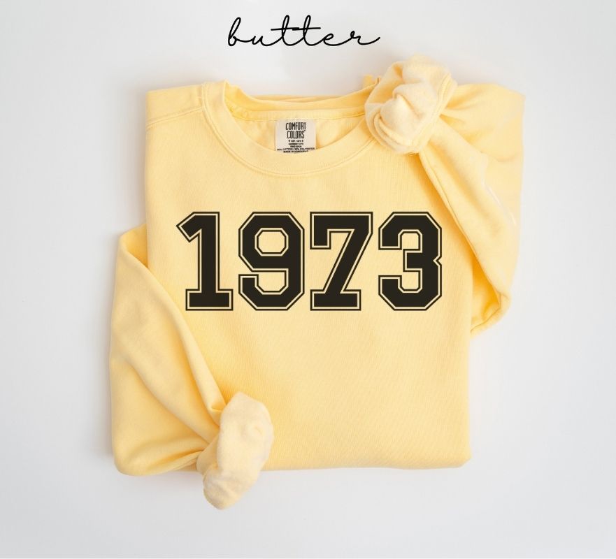 Yellow (butter) sweatshirt with '1973' printed on it, folded and displayed against a white background.