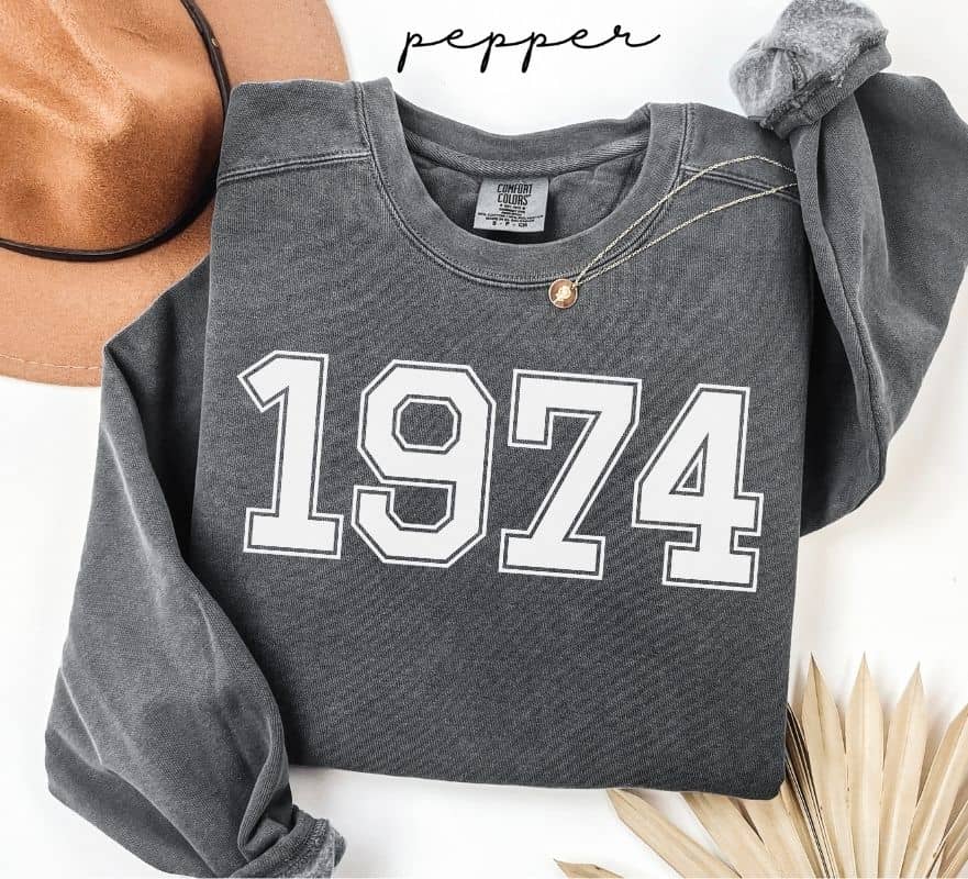 Gray (pepper) sweatshirt with '1974' printed on it, worn by a person, with a plain background.