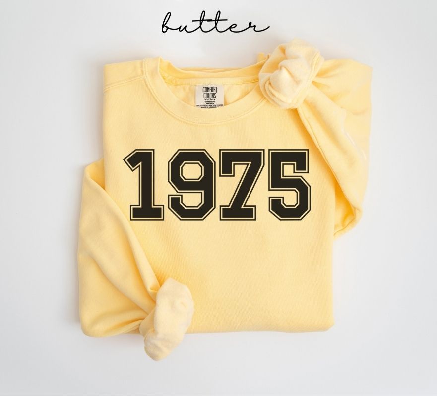 Yellow (butter) sweatshirt with '1975' printed on it, folded and displayed against a white background.