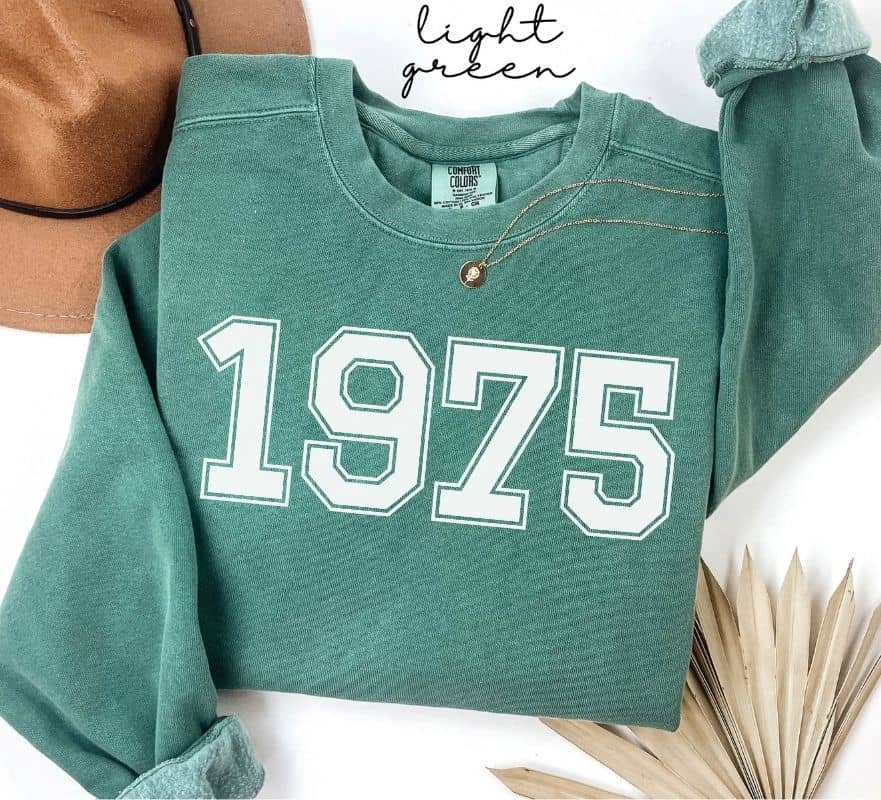 Light green sweatshirt with '1975' printed on it, displayed on a white background.