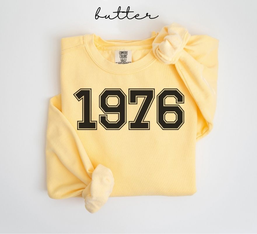 Yellow (butter) sweatshirt with '1976' printed on it, folded and displayed against a white background.
