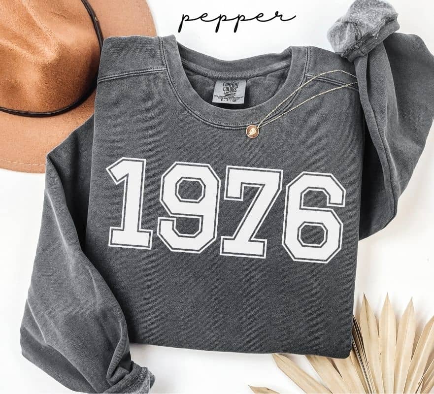 Gray (pepper) sweatshirt with '1976' printed on it, worn by a person, with a plain background.
