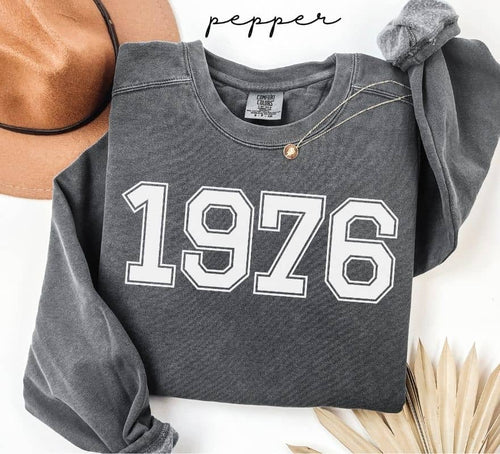 Gray (pepper) sweatshirt with '1976' printed on it, worn by a person, with a plain background.