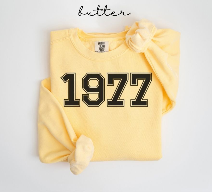 Yellow (butter) sweatshirt with '1977' printed on it, folded and displayed against a white background.