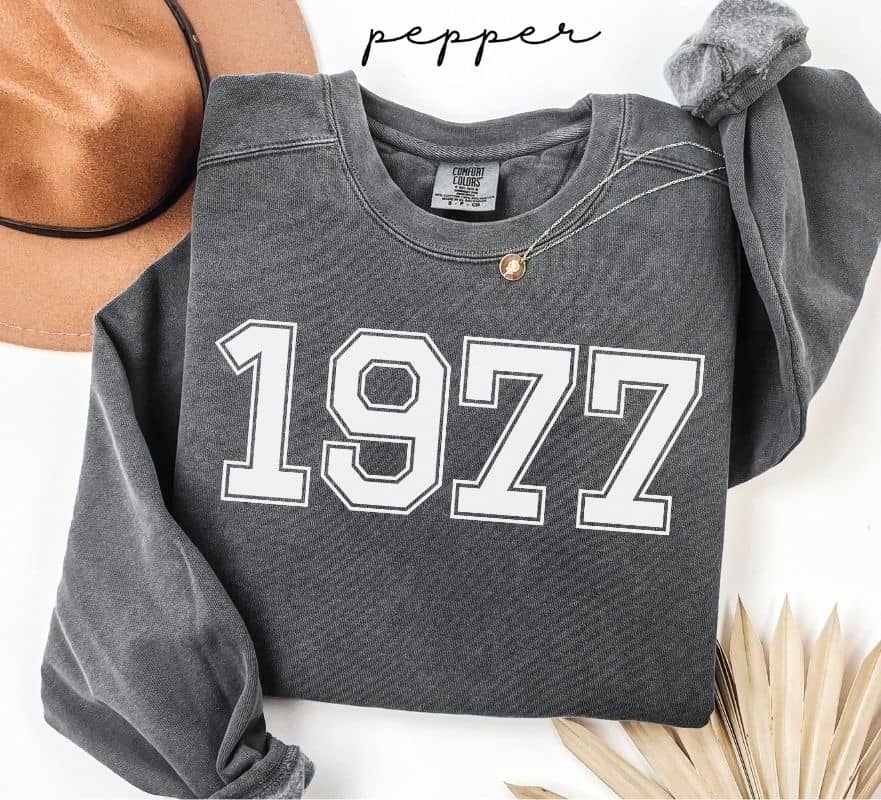 Gray (pepper) sweatshirt with '1977' printed on it, worn by a person, with a plain background.