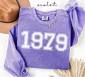 Purple (violet) sweatshirt with '1979' printed on it, worn by a person, with a plain background.