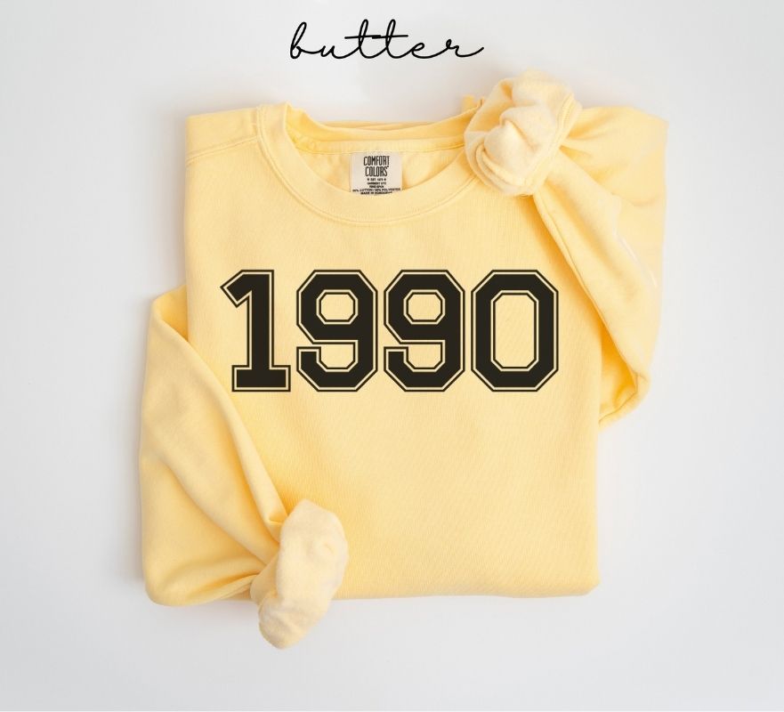 Yellow (butter) sweatshirt with '1990' printed on it, on a light gray background