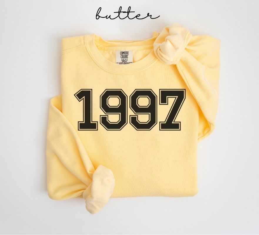 Yellow (butter) sweatshirt with '1997' printed on it, folded and displayed against a white background.
