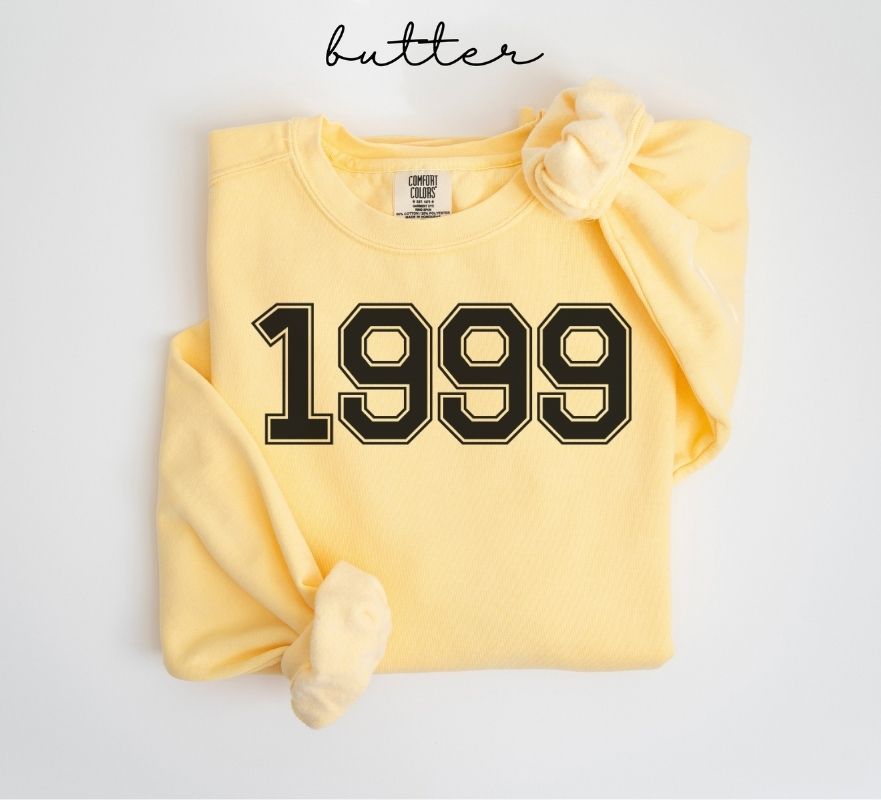Yellow (butter) sweatshirt with '1999' printed on it, folded and displayed against a white background.
