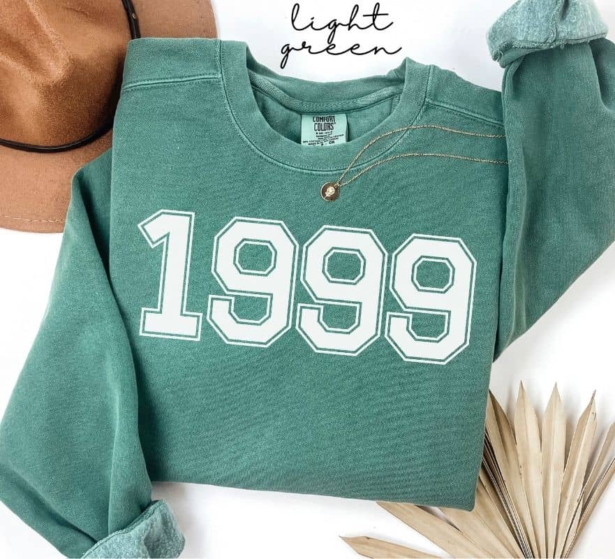 Light green sweatshirt with '1999' printed on it, displayed on a white background.
