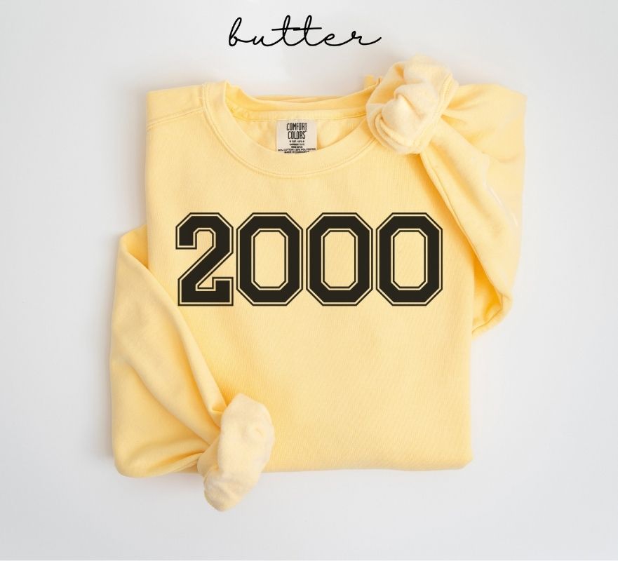 Yellow (butter) sweatshirt with '2000' printed on it, folded and displayed against a white background.
