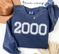 Blue (true navy) sweatshirt with '2000' printed on it, displayed with a hat and decorative elements.
