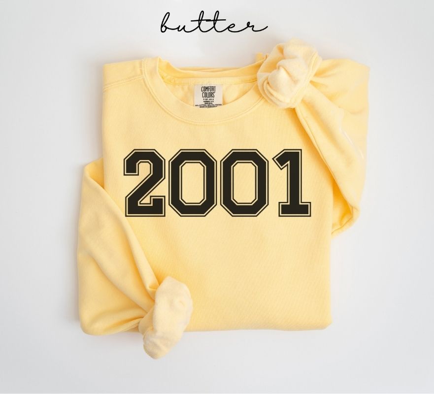 Yellow (butter) sweatshirt with '2001' printed on it, folded and displayed against a white background.
