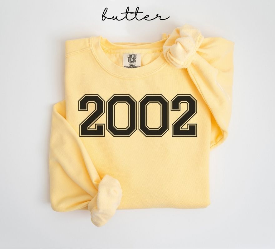 Yellow (butter) sweatshirt with '2002' printed on it, folded and displayed against a white background.
