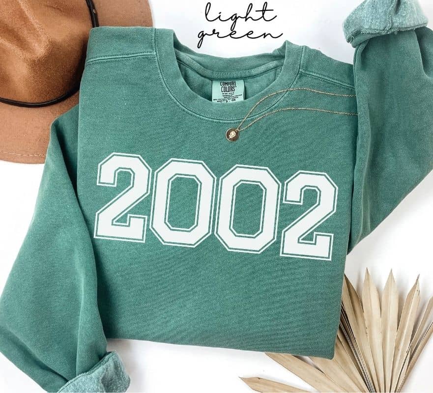 Light green sweatshirt with '2002' printed on it, displayed on a white background.
