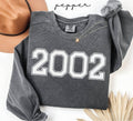Gray (pepper) sweatshirt with '2002' printed on it, worn by a person, with a plain background.
