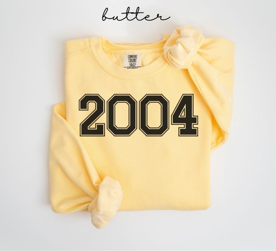 Yellow (butter) sweatshirt with '2004' printed on it, folded and displayed against a white background.
