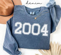 Blue (denim) sweatshirt with '2004' printed on it, worn by a person, with a plain background.
