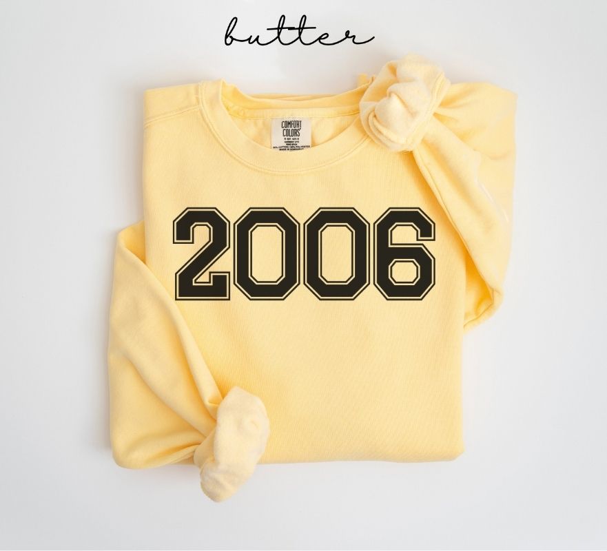 Yellow (butter) sweatshirt with '2006' printed on it, folded and displayed against a white background.
