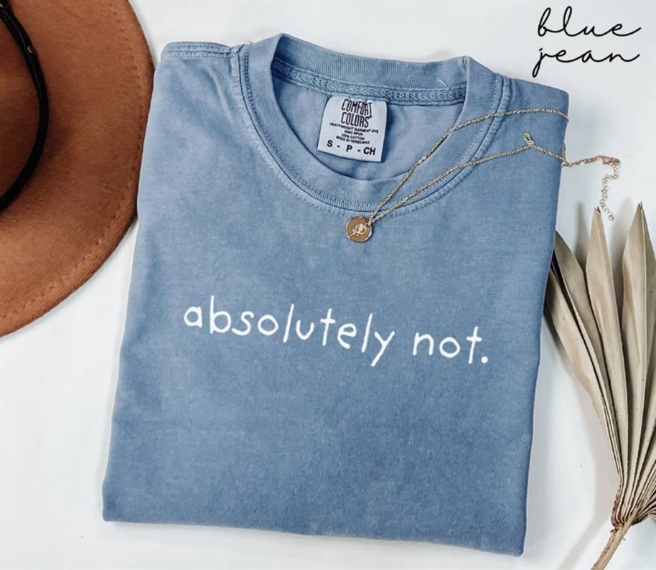 A folded blue jean t-shirt with the text 'Absolutely not.' surrounded by a hat and dried leaves on a white background.