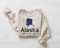 Beige (Sand) sweatshirt with blue Alaska map and flag outline and text "Alaska is calling I must go" on a white background