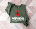 Military green sweatshirt with red map of Albania and text on a wooden floor