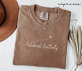 Folded brown t-shirt with the text 'Antisocial Butterfly', accompanied by a necklace and hat, on a white background.