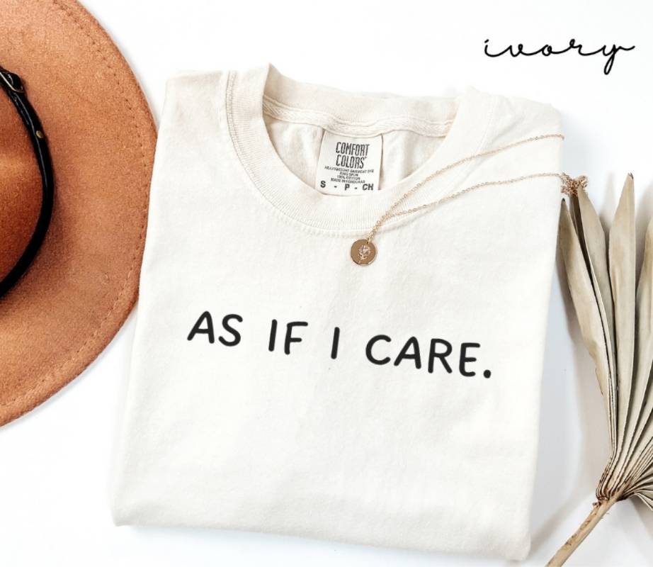 White T-shirt with the text 'AS IF I CARE,' a brown hat, and a dried plant on a white background.