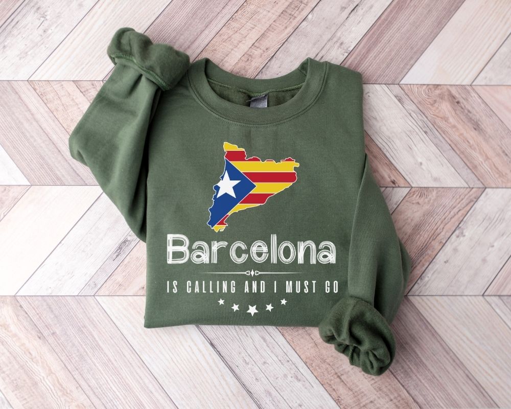 A millitray green sweatshirt featuring a Barcelona design is placed on a wooden floor.