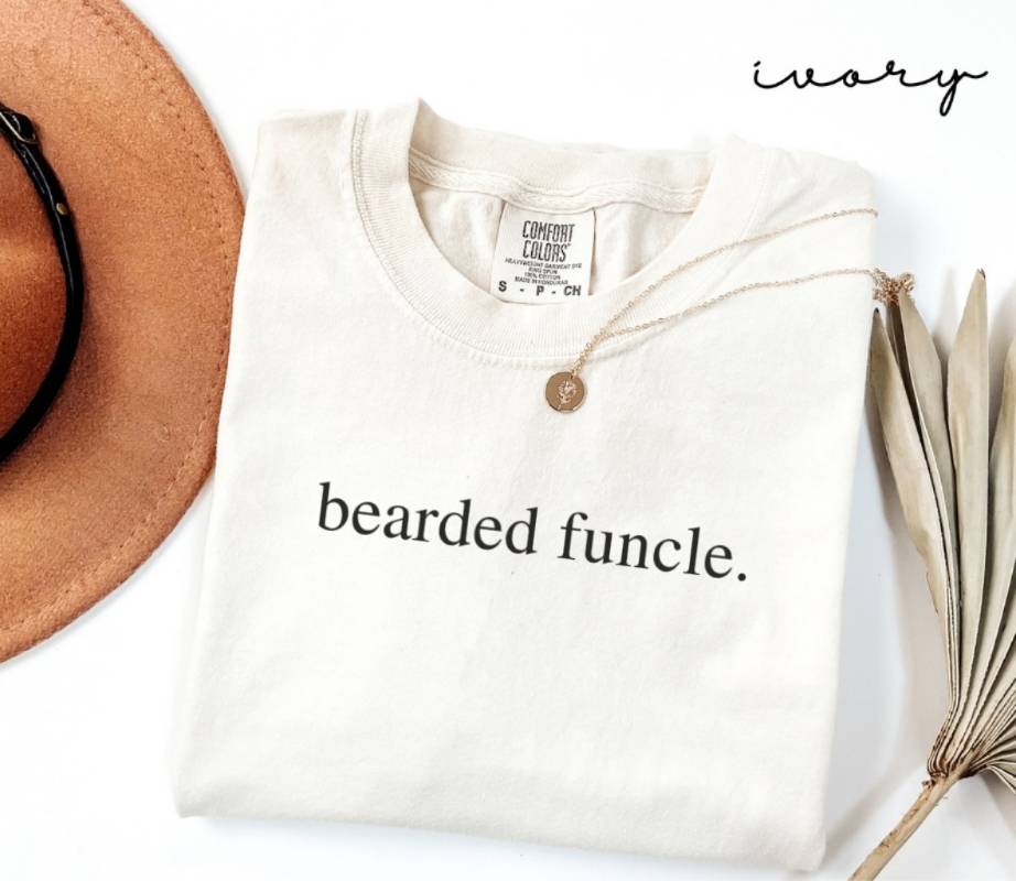 White t-shirt with the text 'Bearded Funcle,' a brown hat, and a dried plant on a white background.