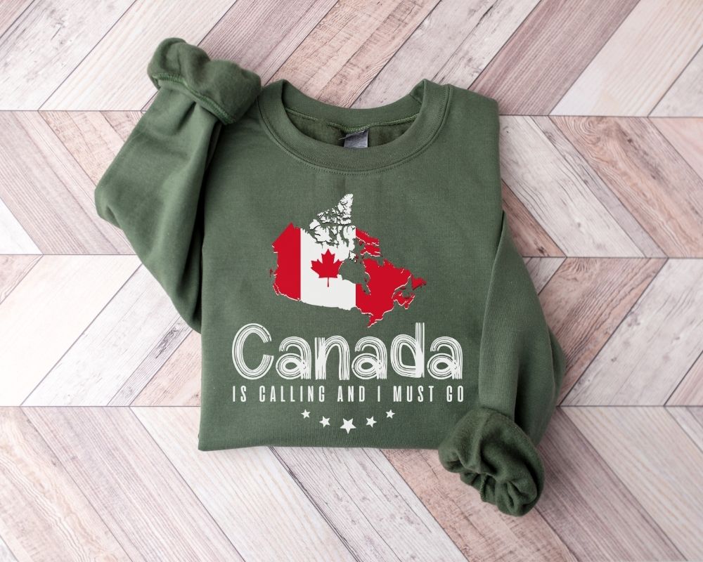 A military green sweatshirt featuring a map of Canada and accompanying text, placed on a wooden floor.