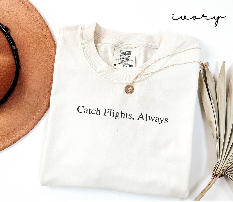 White (ivory) t-shirt with 'Catch Flights, Always' text, brown hat, and dried plant on a white background