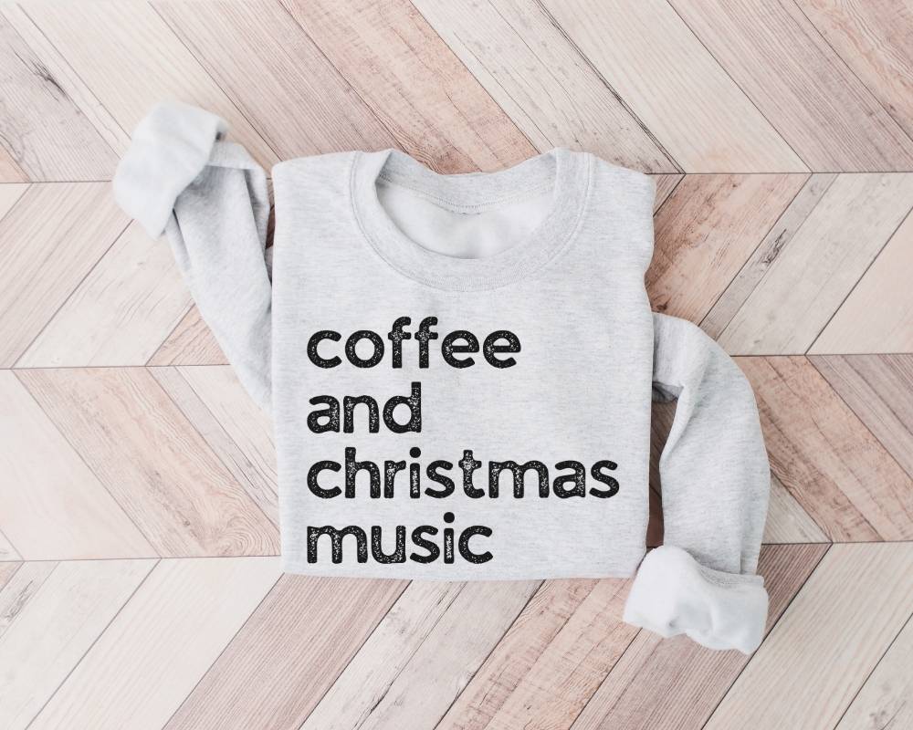 White (ash) sweatshirt with 'coffee and christmas music' text on a wooden floor