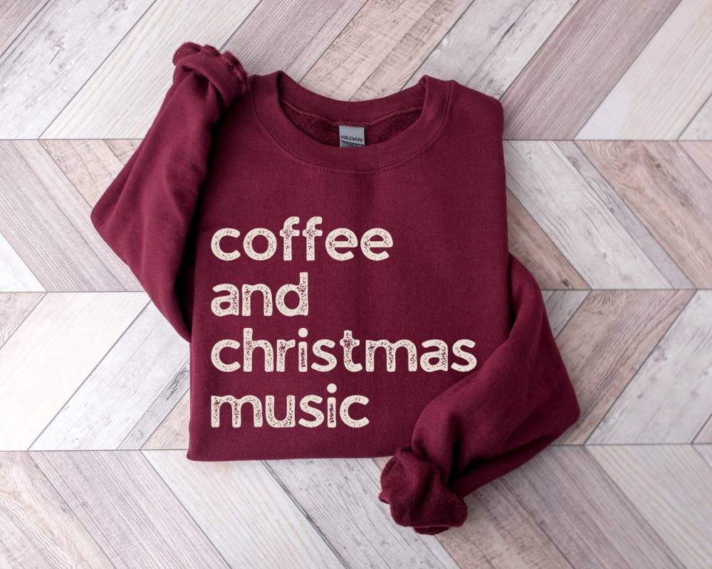 Maroon sweatshirt with 'coffee and christmas music' text on a wooden floor