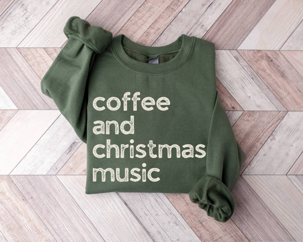 Military green sweatshirt with 'coffee and christmas music' text on a wooden floor
