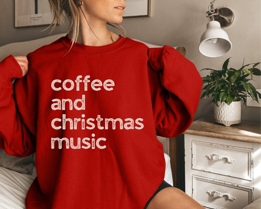 Person wearing a red sweatshirt with 'coffee and christmas music' text in a bedroom setting.