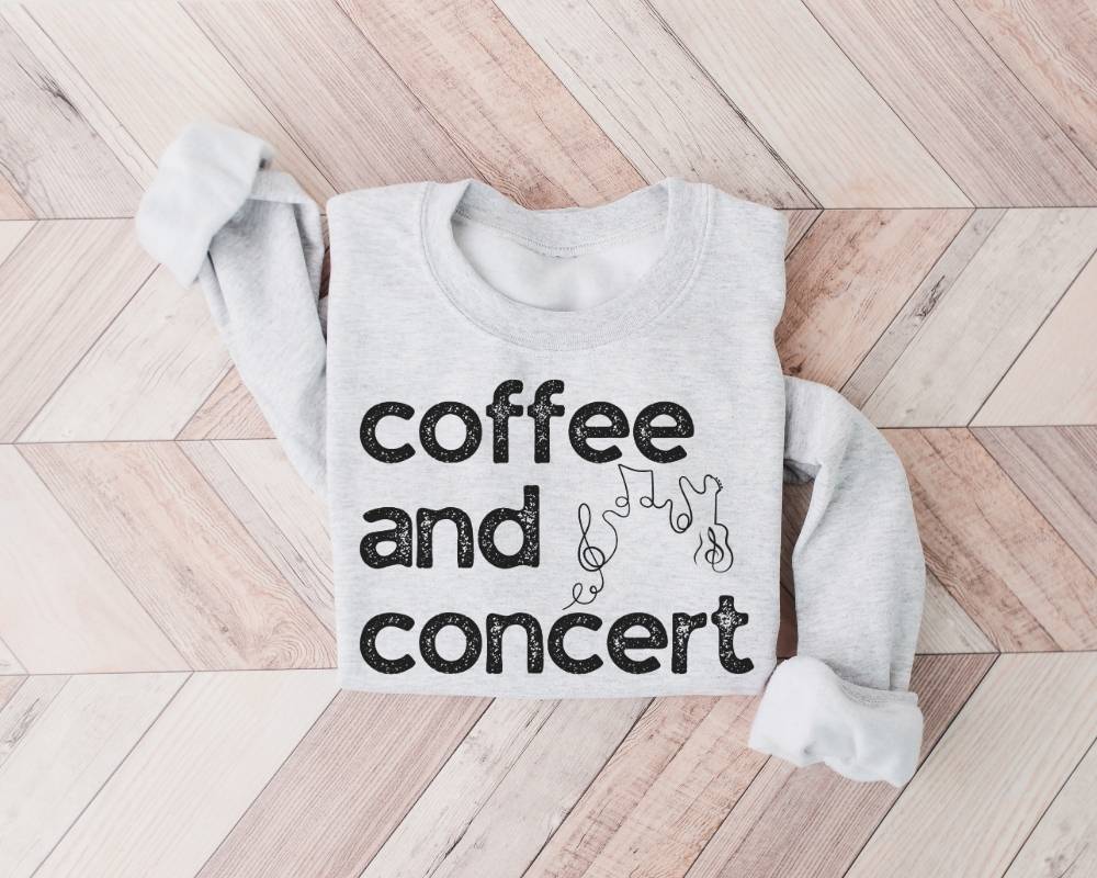 White (ash) sweatshirt with 'coffee and concert' text on a wooden floor