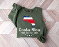A millitray green sweatshirt featuring a map of Costa Rica and text displayed on a wooden floor.