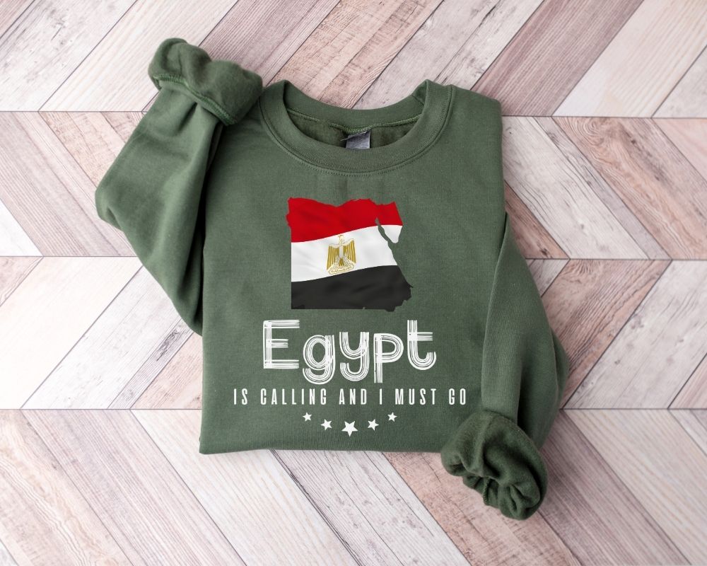 A millitray green sweatshirt featuring an Egyptian flag design and text, placed on a wooden floor.