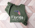 A military green sweatshirt featuring a Florida design is laid out on a wooden floor.