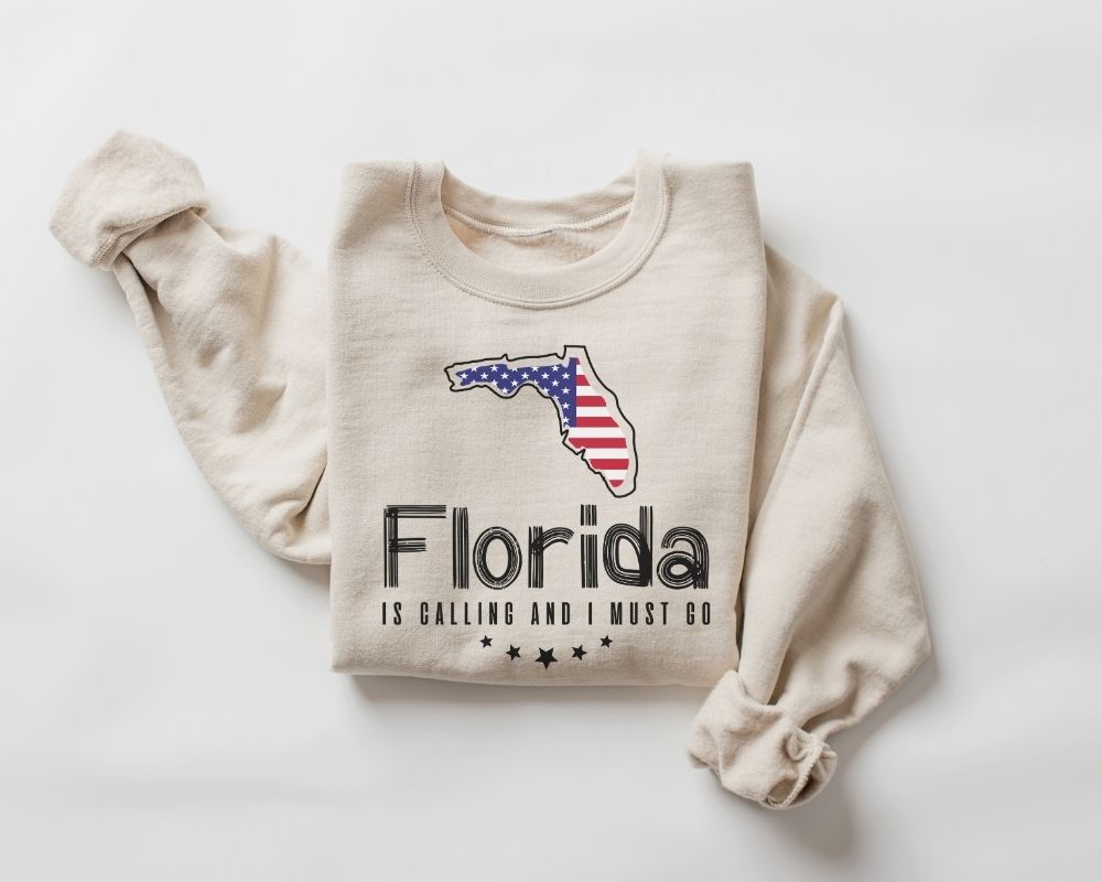 A beige (sand) sweatshirt featuring a Florida map and text design against a white background.