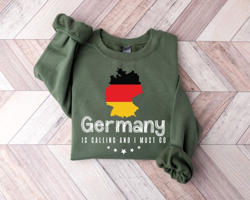 A millitray green sweatshirt featuring a design of the German flag and text, placed on a wooden floor.