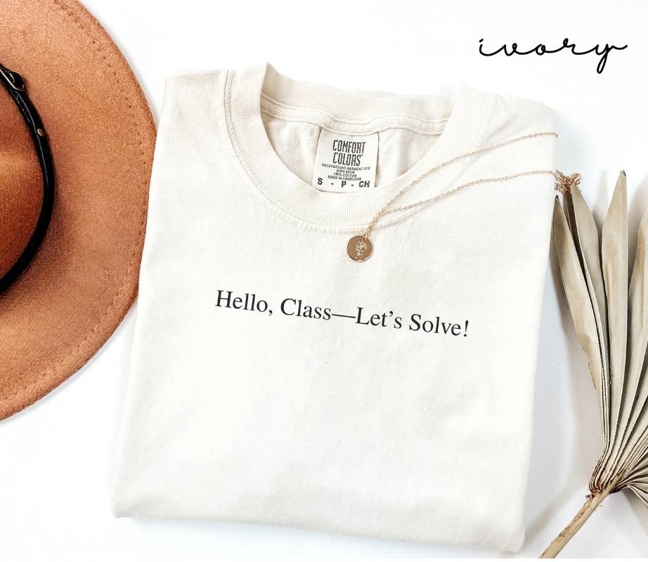 White (ivory) t-shirt with 'Hello, Class—Let's Solve!' text, brown hat, necklace, and dried plant on a white background.