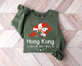 Military green sweatshirt with red and white design on a wooden floor
