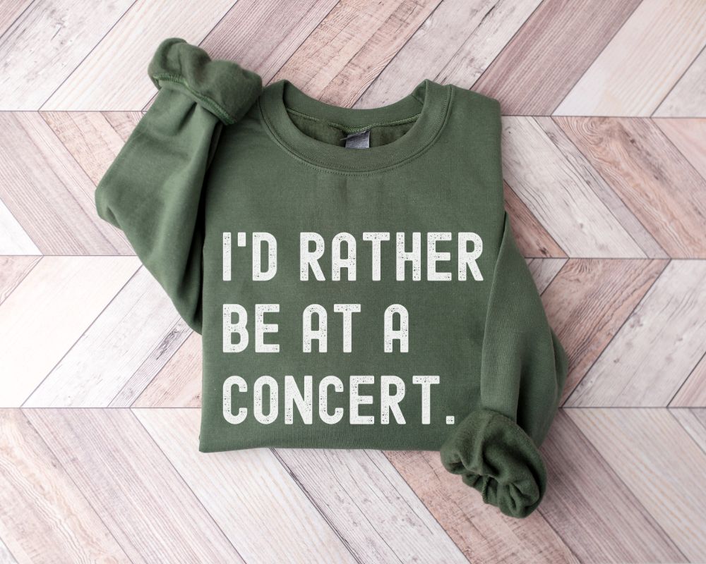 Military green sweatshirt with text 'I'd Rather Be at a Concert' on the flooring