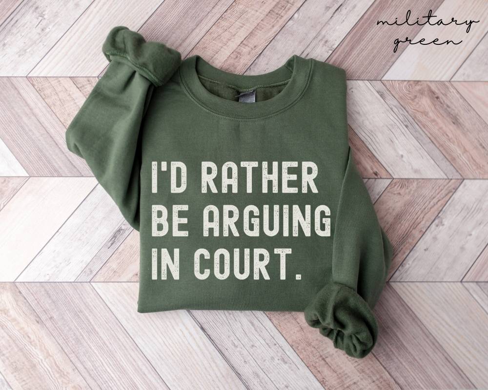 Military green sweatshirt with text 'I'd rather be arguing in court' on a wooden floor.